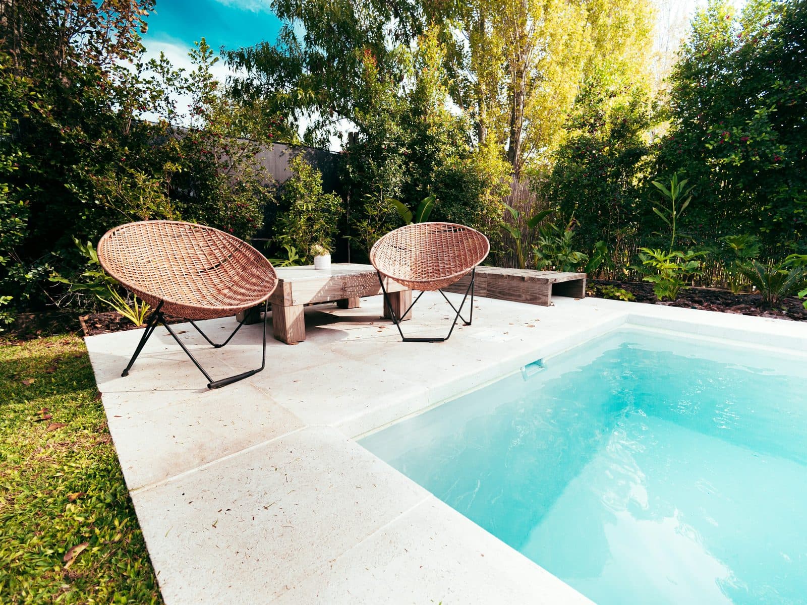 A small rectangular plunge pool with a limestone deck and two wicker chairs, surrounded by trees.