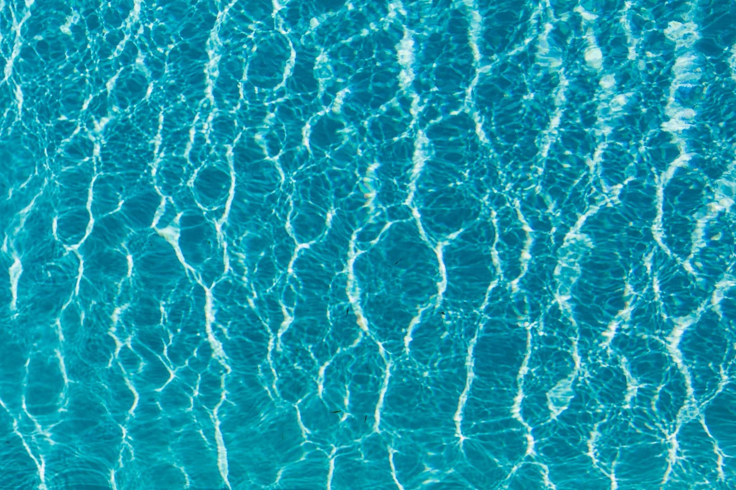 Straight-down view of clear pool water with bright sunlight patterns rippling across the floor.