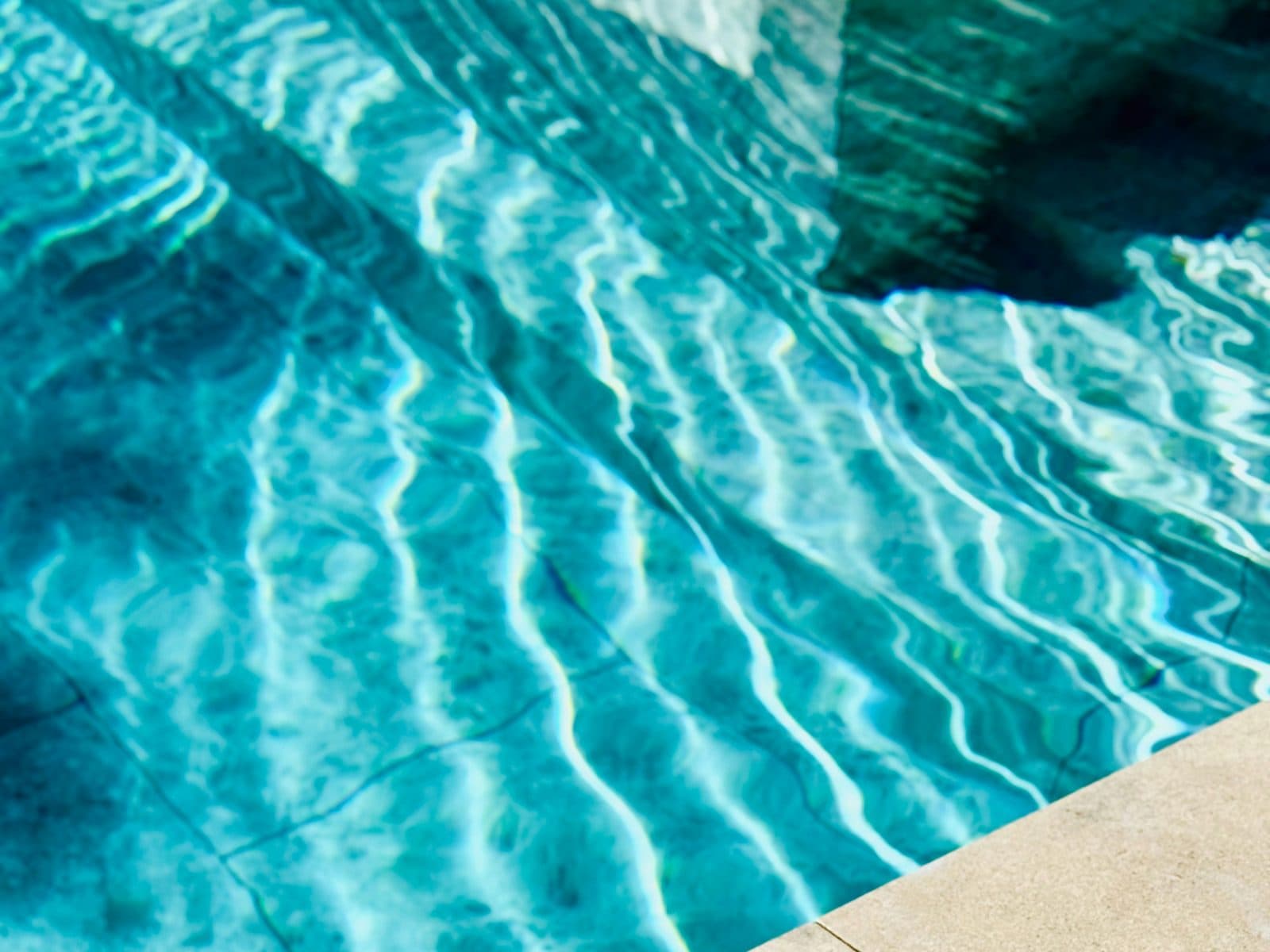 Clear pool water with sunlight patterns over wide limestone steps leading down from a tanning ledge.
